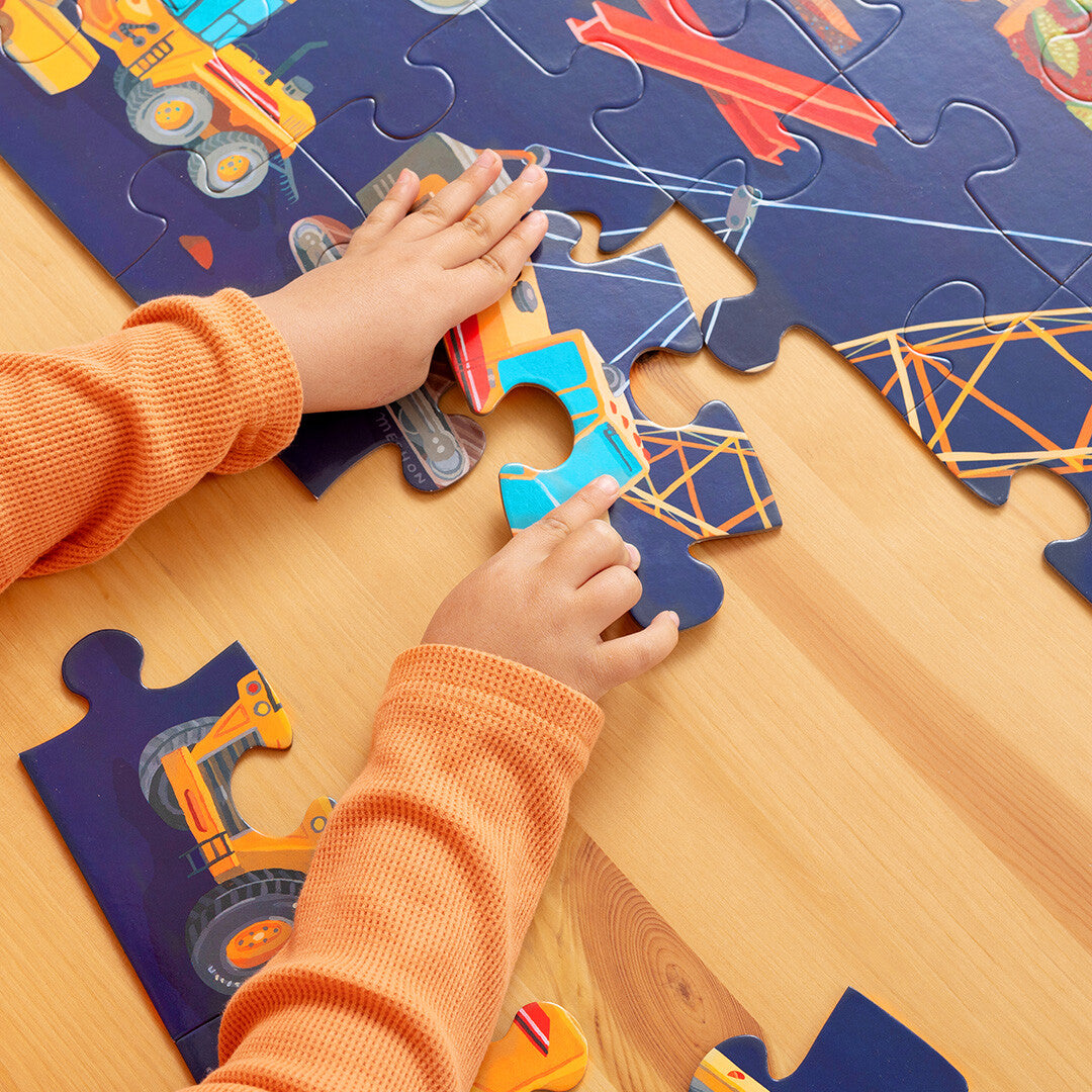 Kinderhanden leggen een stukje van de bouwplaats vloerpuzzel met voertuigen.
