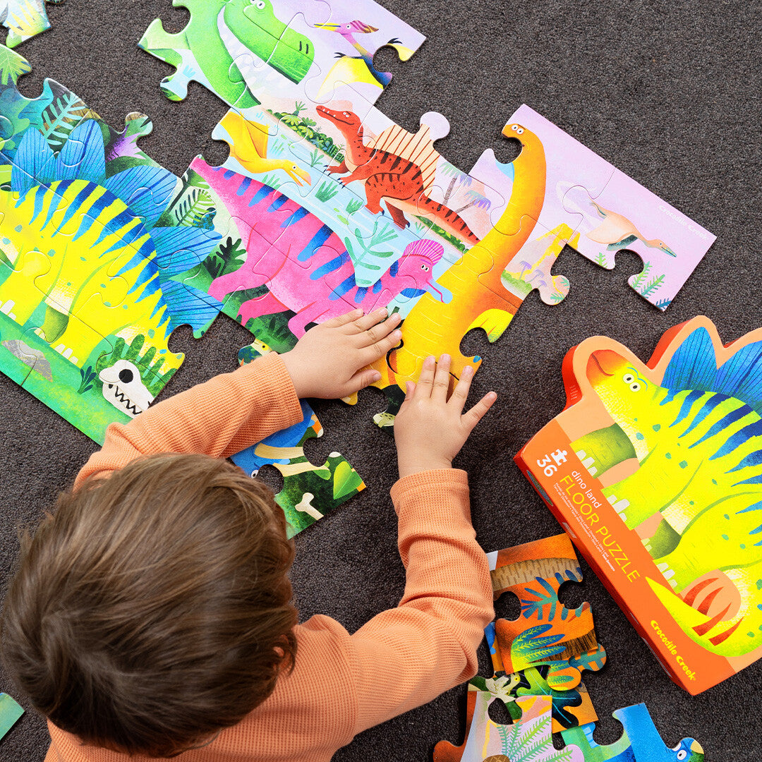 Een kind legt een Crocodile Creek vloerpuzzel met dinosaurussen op de grond.