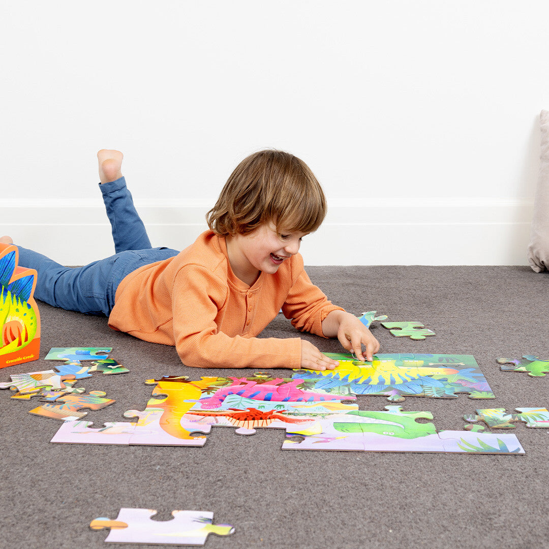 Een lachend kind legt een Crocodile Creek vloerpuzzel met dinosaurussen op de grond.