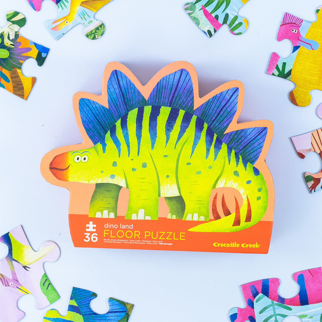 Crocodile Creek vloerpuzzel Dino Land verpakking in de vorm van een groene stegosaurus, omringd door losse puzzelstukken.