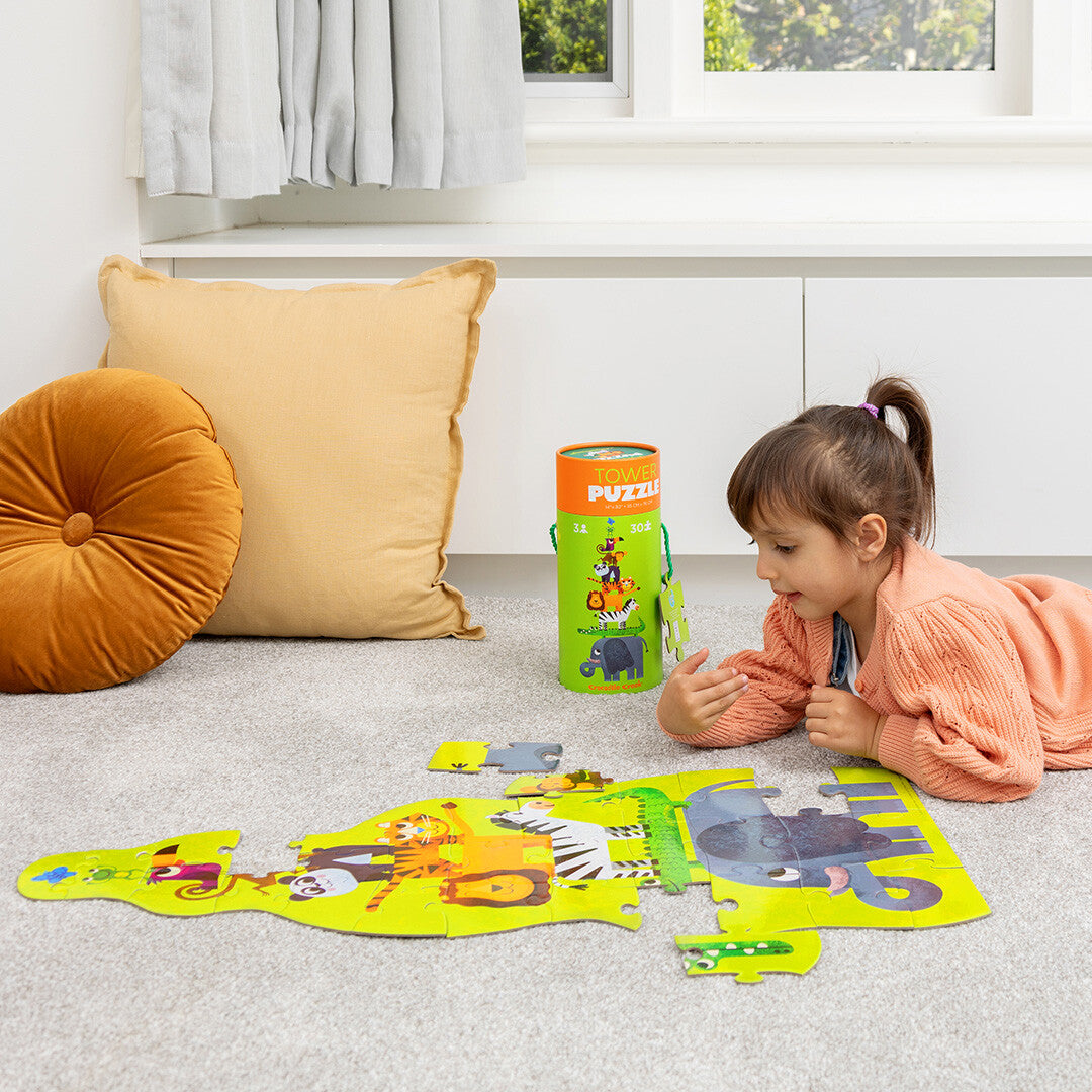 Een kind ligt op de vloer en kijkt naar de deels gelegde Crocodile Creek vloerpuzzel met jungle dieren.