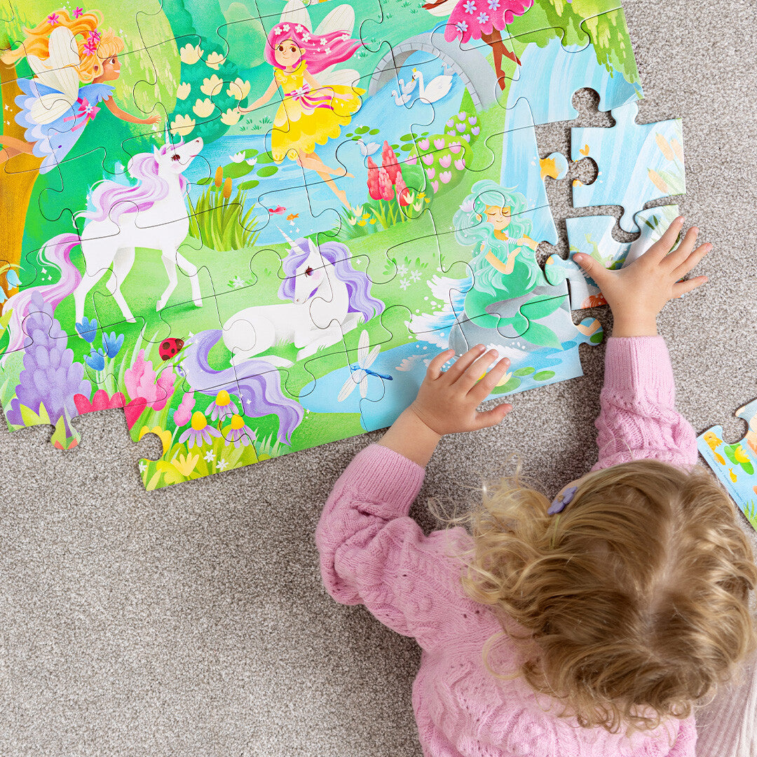 Een kind legt een stukje van de Crocodile Creek vloerpuzzel met magische vriendjes op een grijze vloer.