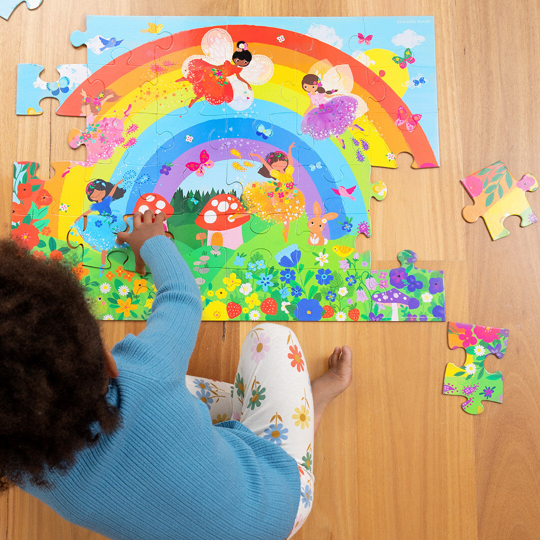 Een kind legt een puzzelstukje in de Crocodile Creek vloerpuzzel met een regenboog en feeën.