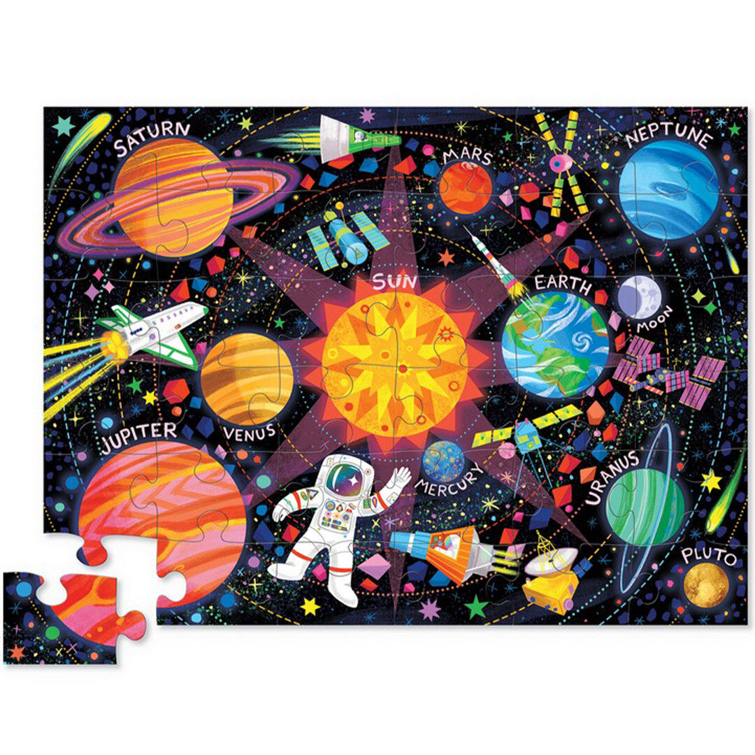 Crocodile Creek vloerpuzzel met een afbeelding van het zonnestelsel, planeten, raketten en een astronaut, met één losse puzzelstuk.