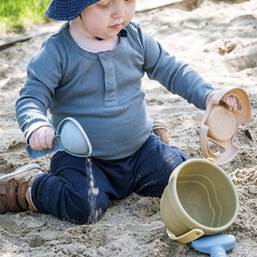 Een baby speelt in de zandbak met een schep en de zandset.