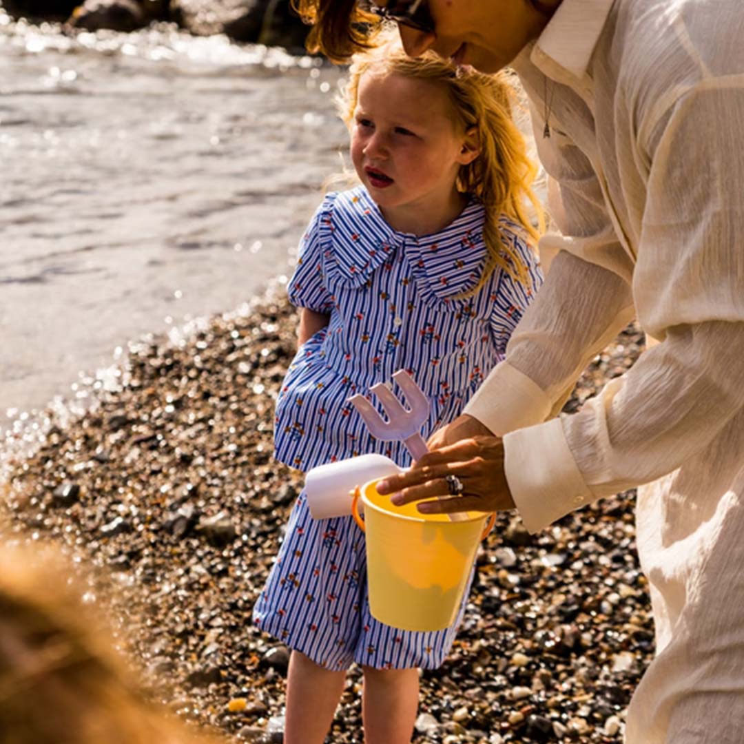 Een kind en volwassene spelen met de Dantoy zandset op een kiezelstrand.