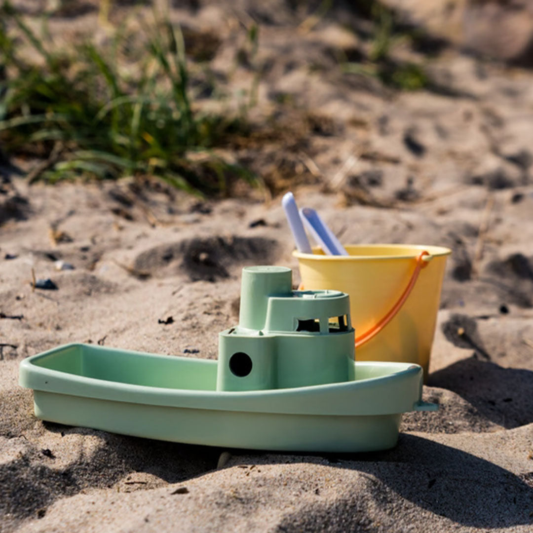 De Dantoy groene boot en gele emmer van de zandset staan op een zandstrand.
