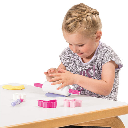 Een meisje speelt met een roze deegroller en uitsteekvormpjes van de dantoy speelgoed bakset op een witte tafel.
