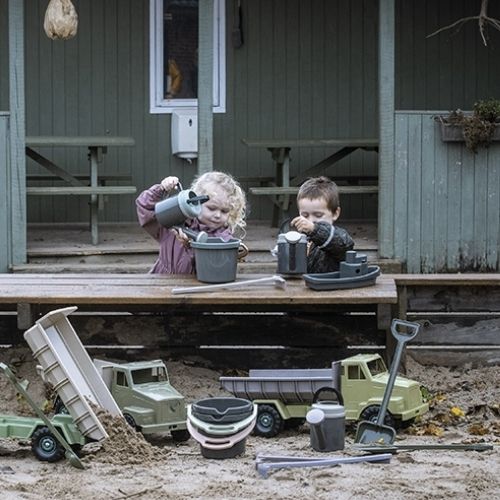 Twee kinderen spelen met dantoy zandspeelgoed, waaronder emmers en vrachtwagens, op een houten veranda.