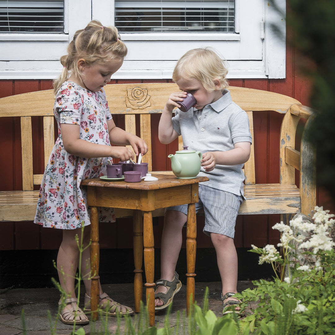 Twee kinderen spelen buiten met het Dantoy theeservies op een houten bankje.