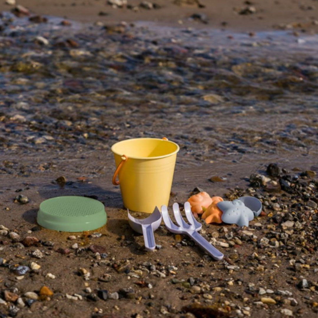 dantoy pastel zandset met emmer en dierenvormpjes op een kiezelstrand bij het water.