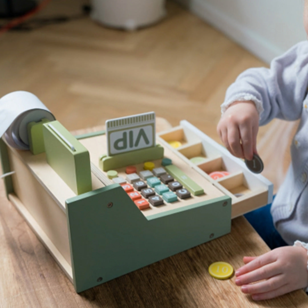 Een kind speelt met de dantoy houten kassa op een tafel, met een houten munt in de hand.