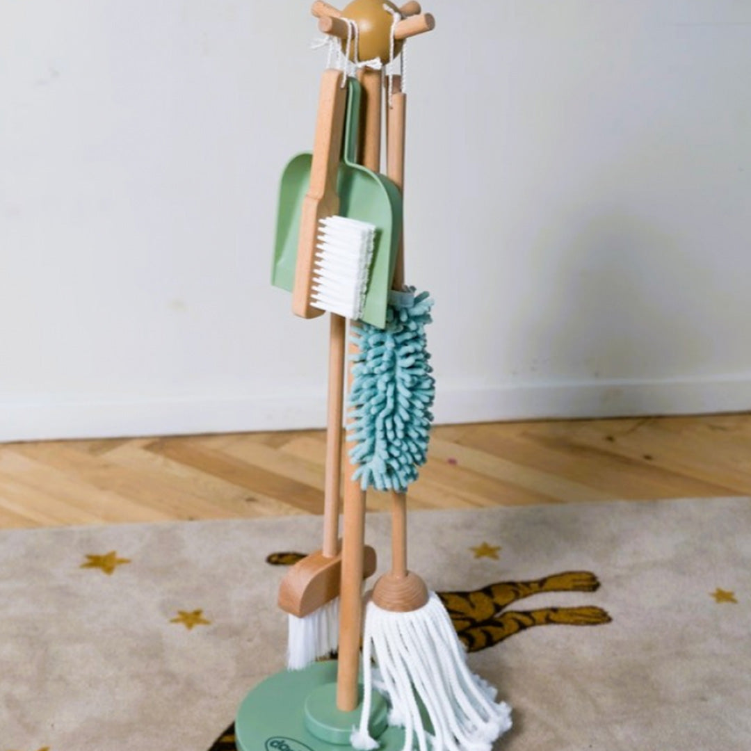 Detail van de dantoy houten speelgoed schoonmaakset met bezem, mop, plumeau, stoffer en blik aan de standaard op een vloerkleed.