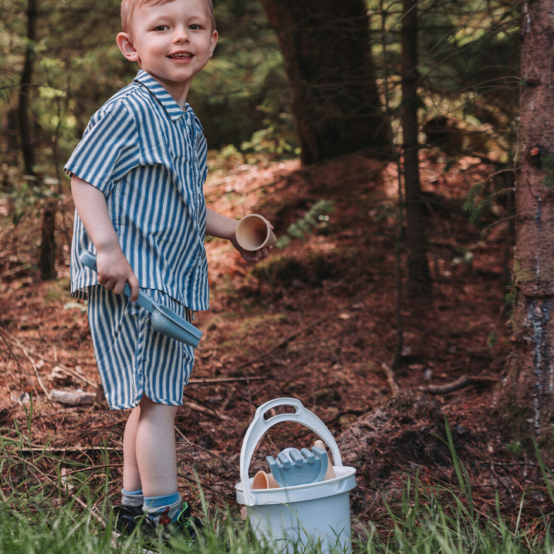 Een jongen speelt in het bos met een Dantoy blauwe zandset, met een schep en een emmer.