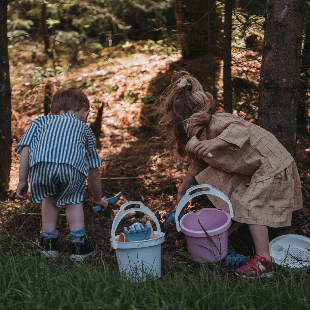 Twee kinderen spelen in het bos met Dantoy zandsets, met emmers en scheppen.
