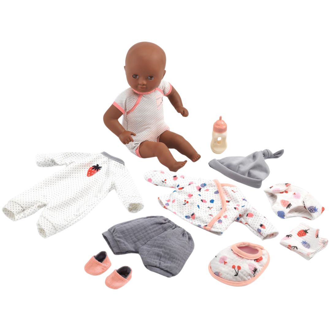 Djeco babypop met donkere huidskleur zittend tussen een collectie poppenkleding en accessoires, waaronder een pyjama, jasje, broekje en fles.