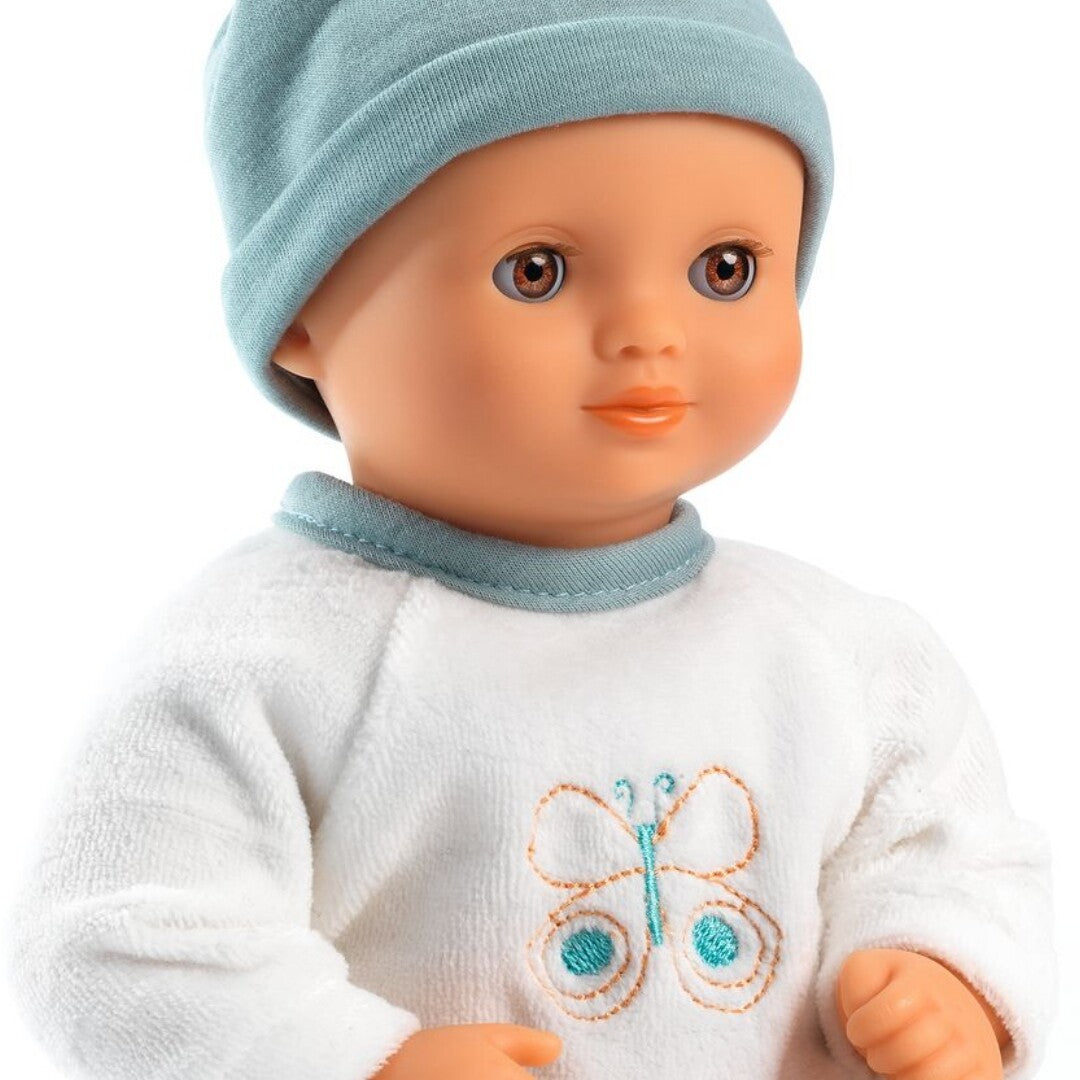 Close-up van de Djeco babypop Pomea met een wit velours rompertje met vlinder en een teal mutsje.