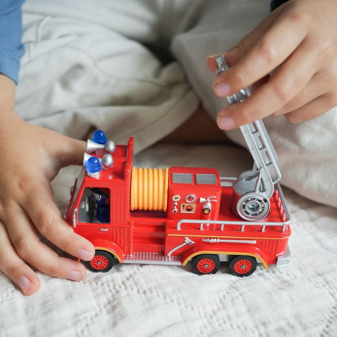 Kinderhanden spelen met de rode Djeco speelgoed brandweerauto Captain Fire, waarbij de ladder wordt uitgeschoven.