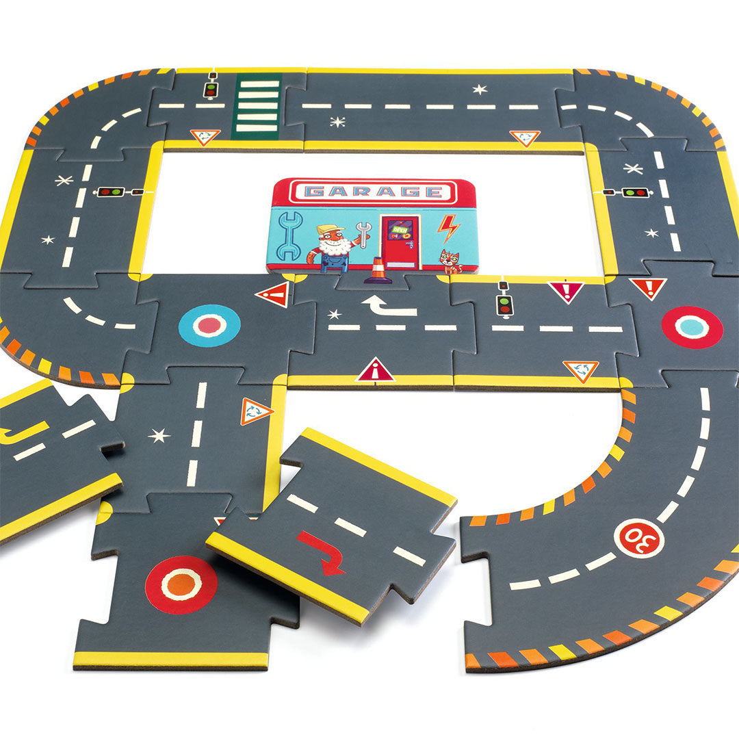 Een gedeeltelijk gelegde Djeco Crazy Motors vloerpuzzel autoweg met een garage in het midden en losse puzzelstukken.