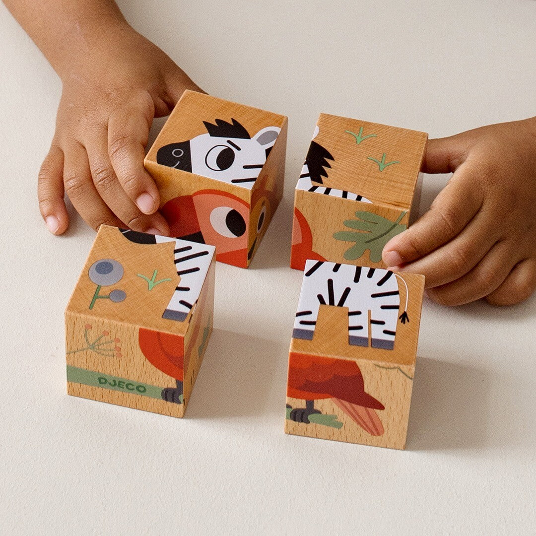 Kinderhanden spelen met vier Djeco houten blokken van de dierenpuzzel, met delen van een zebra en papegaai zichtbaar.
