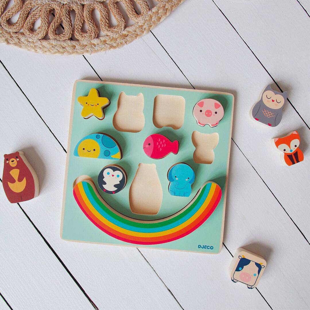Djeco houten puzzelbord met regenboog en dierenstukken, deels in de puzzel en deels ernaast op een witte vloer.