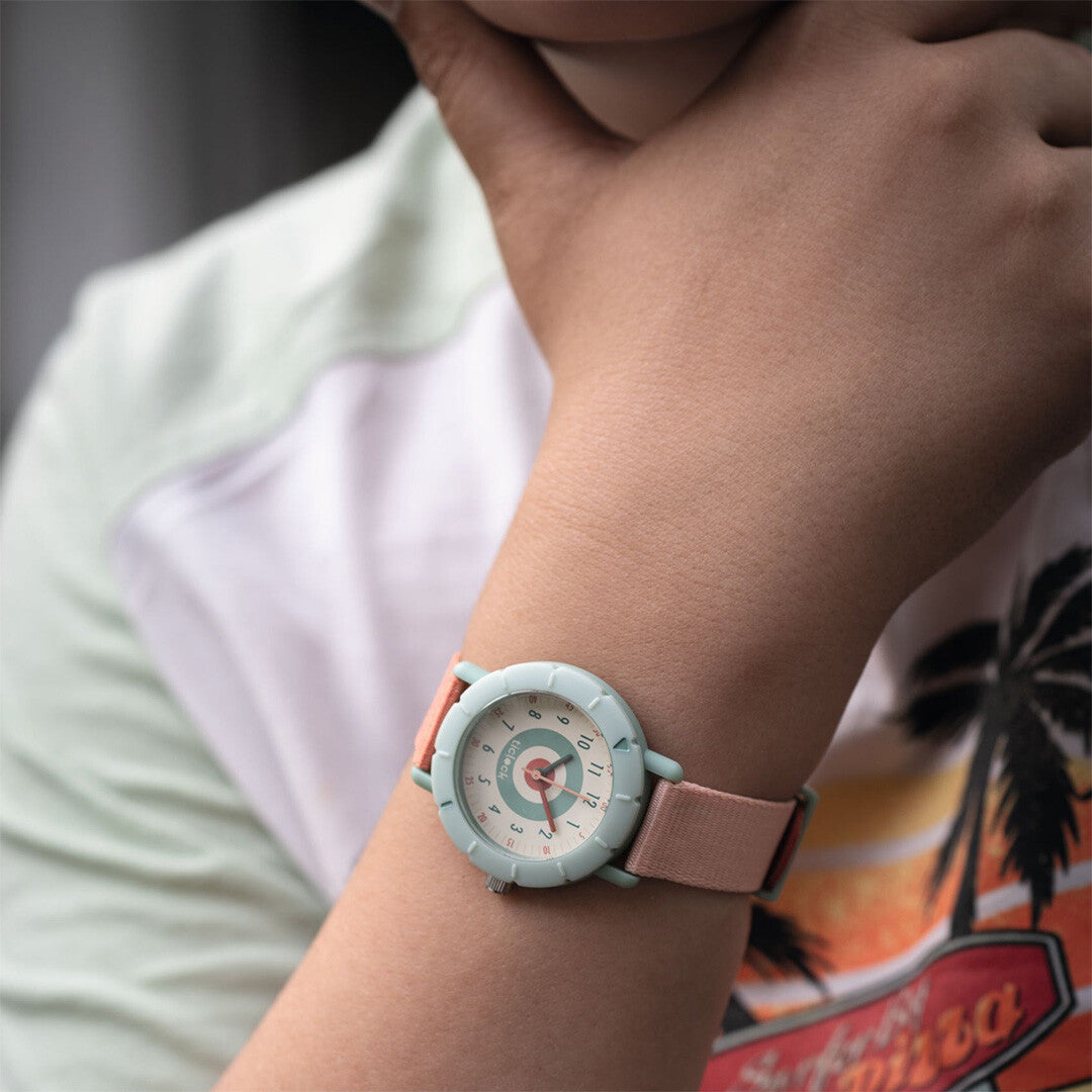 Kinderhorloge met lichtgroene wijzerplaat en roze-rode band om de pols van een kind.