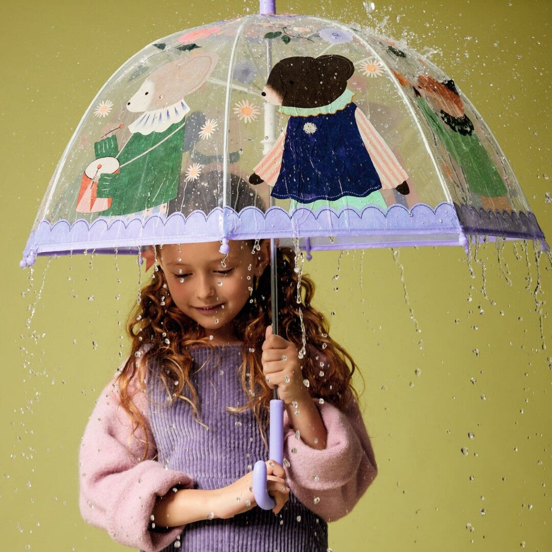 Meisje met krullend haar houdt een Djeco kinderparaplu met dierenmuzikanten vast in de regen.