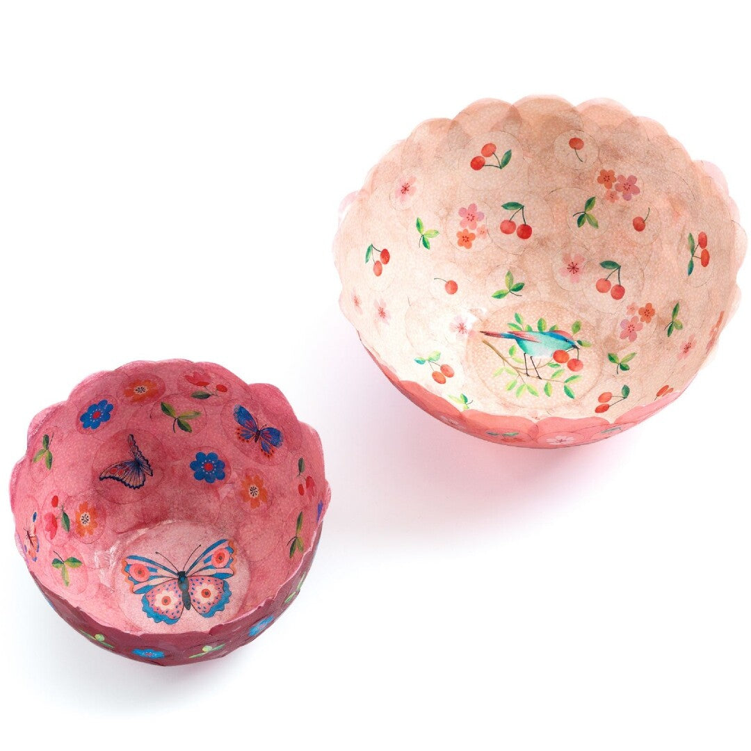 Twee afgewerkte papieren kommen, één roze met vlinders en bloemen, de andere perzikkleurig met kersen en een vogel.