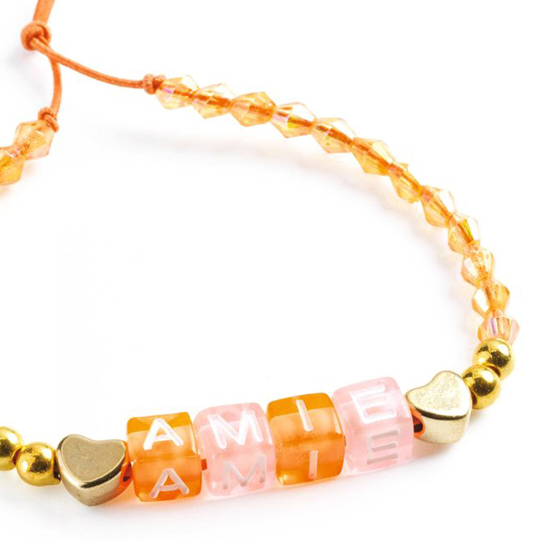 Close-up van een oranje armband gemaakt met de Djeco kralenset, met gouden hartjes en letterkralen die 'AMIE' spellen.