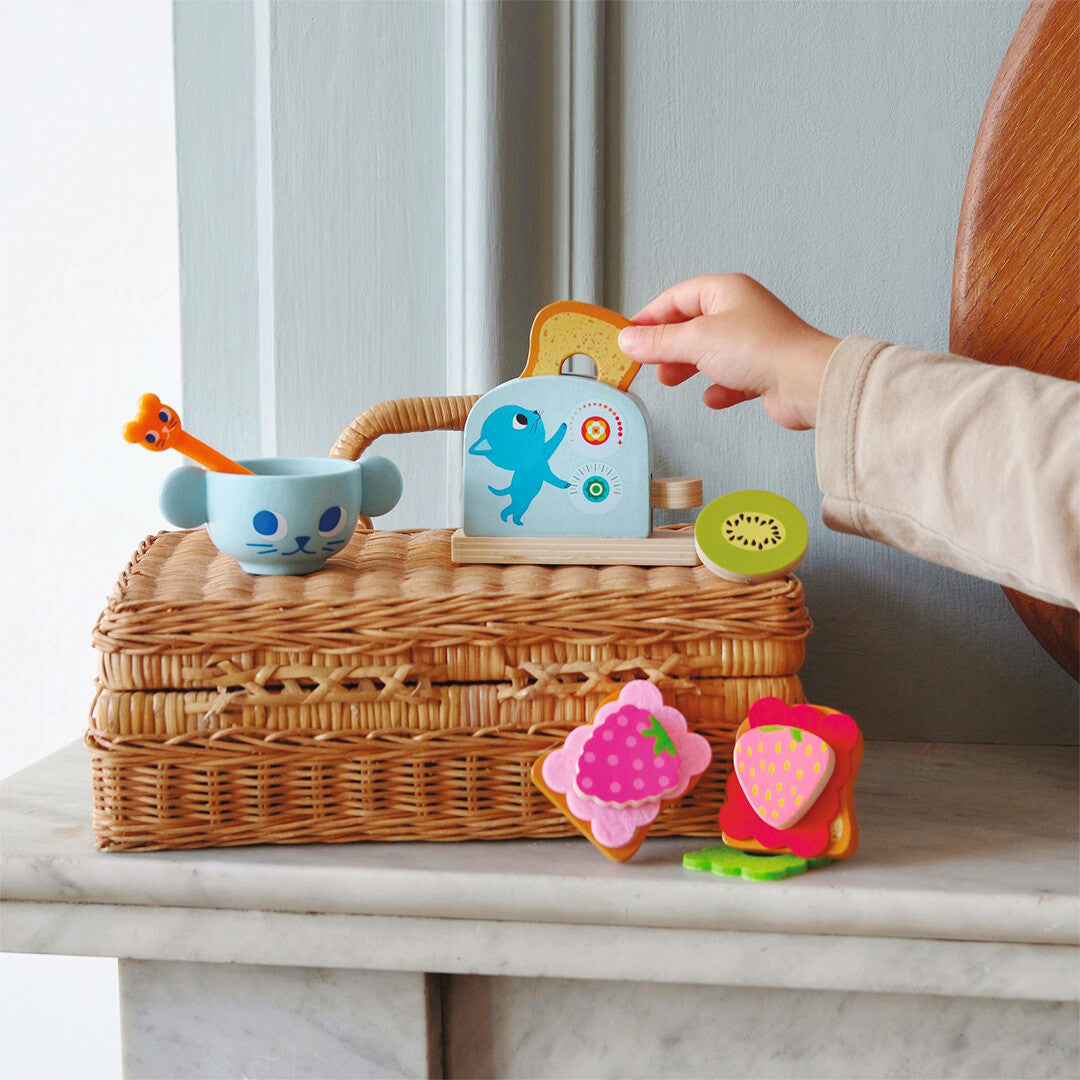 Een kinderhand stopt een houten toastje in de Djeco speelgoedbroodrooster van de kattenontbijtset.