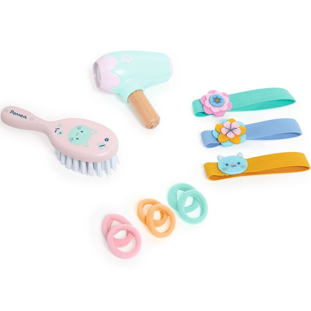 De Djeco Pomea poppen haarstyling set met roze borstel, mintgroene föhn, haarbanden en elastiekjes.