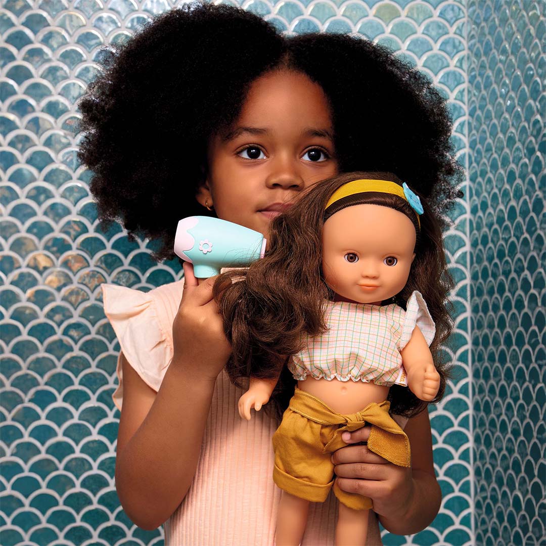 Een kind houdt een pop vast en gebruikt de mintgroene speelgoedföhn uit de Djeco Pomea haarstyling set.