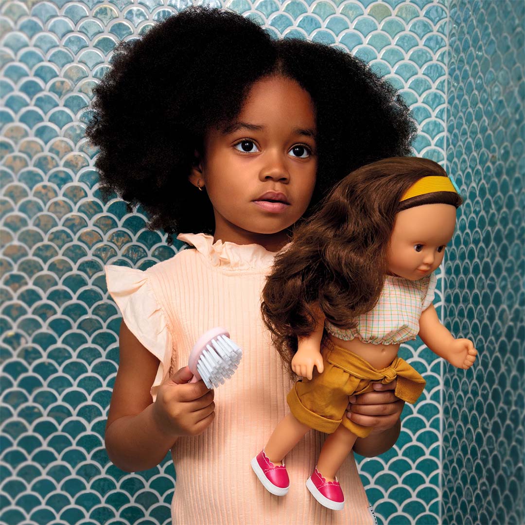 Een kind borstelt het haar van een pop met de roze borstel uit de Djeco Pomea poppen haarstyling set.
