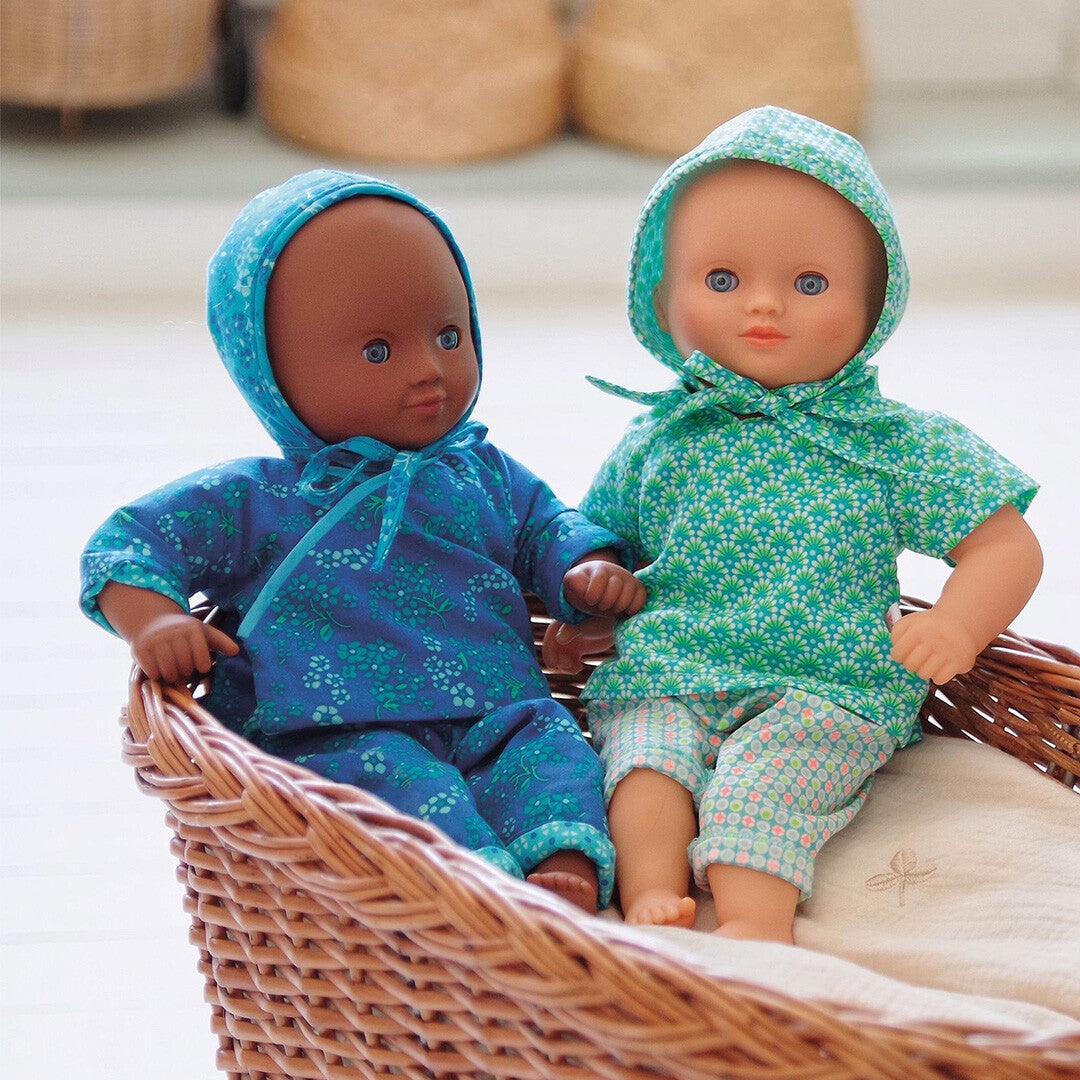 Twee poppen in een mand, waarvan één de Djeco blauw gebloemde poppenkledingset draagt.