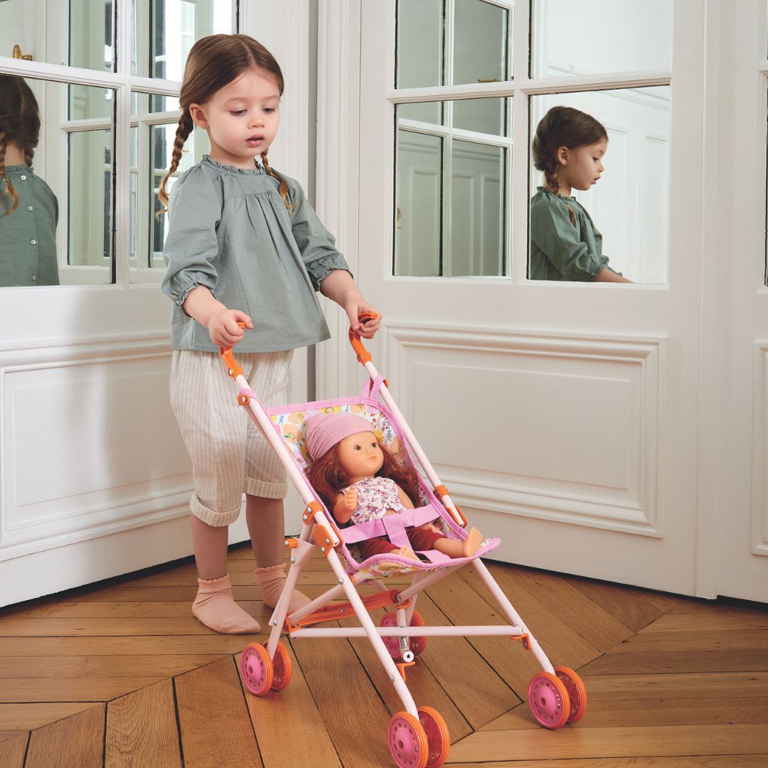 Een meisje duwt een roze poppenbuggy met een pop erin.