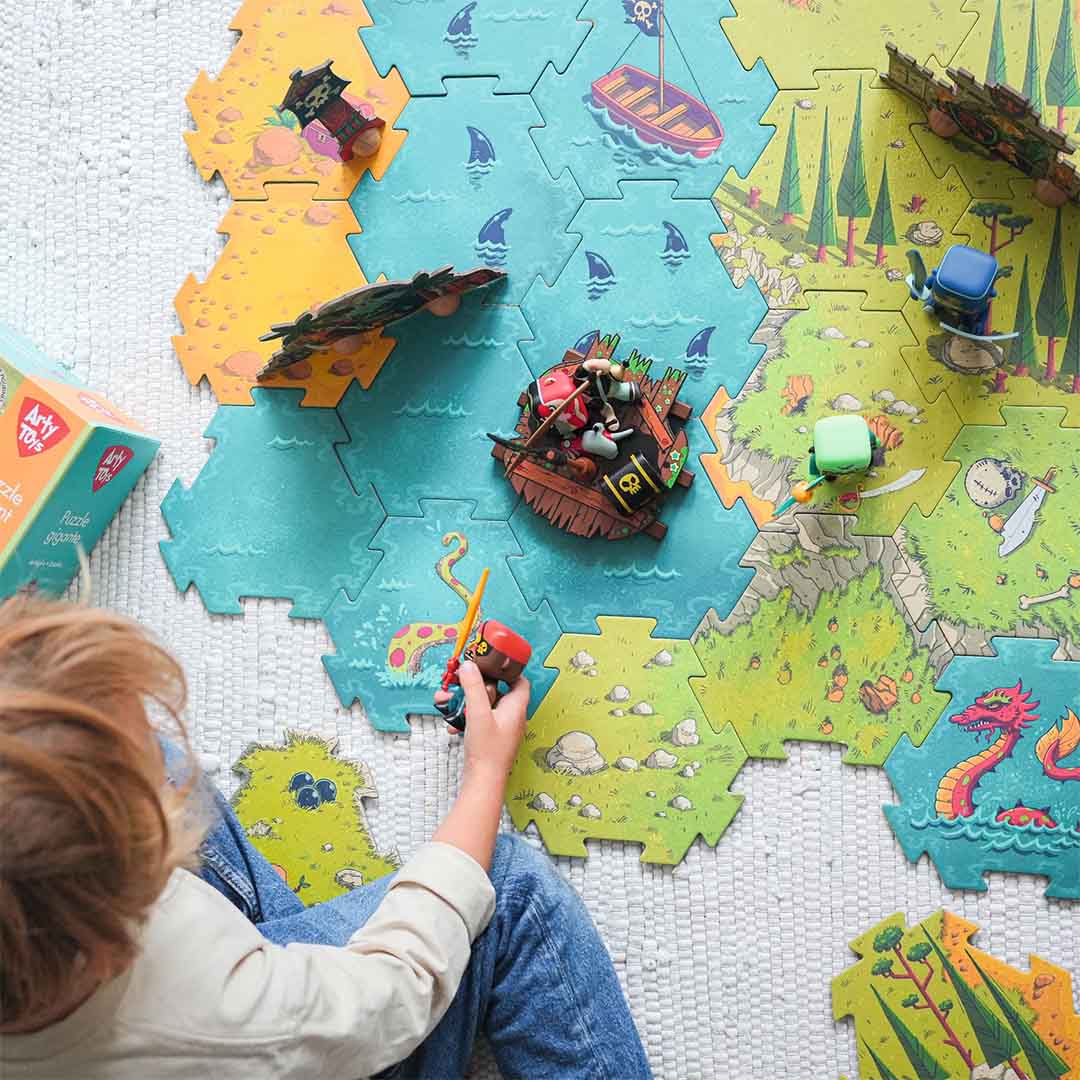Detailopname van een kind dat speelt met de Djeco Arty Toys reuze puzzel, met een piratenschip en een eiland met een schedelgrot.