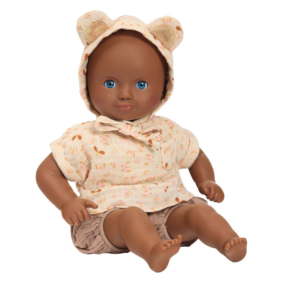 Djeco babypop met donkere huidskleur, blauwe ogen, zittend in een gebloemd shirt met berenmuts en bruine broek.