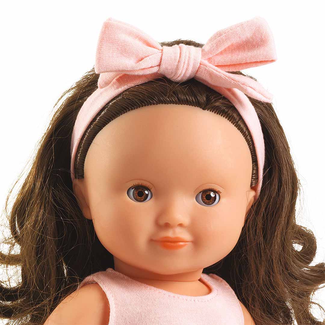 Close-up van het gezicht van de babypop Roxane met bruine ogen en een roze hoofdband.