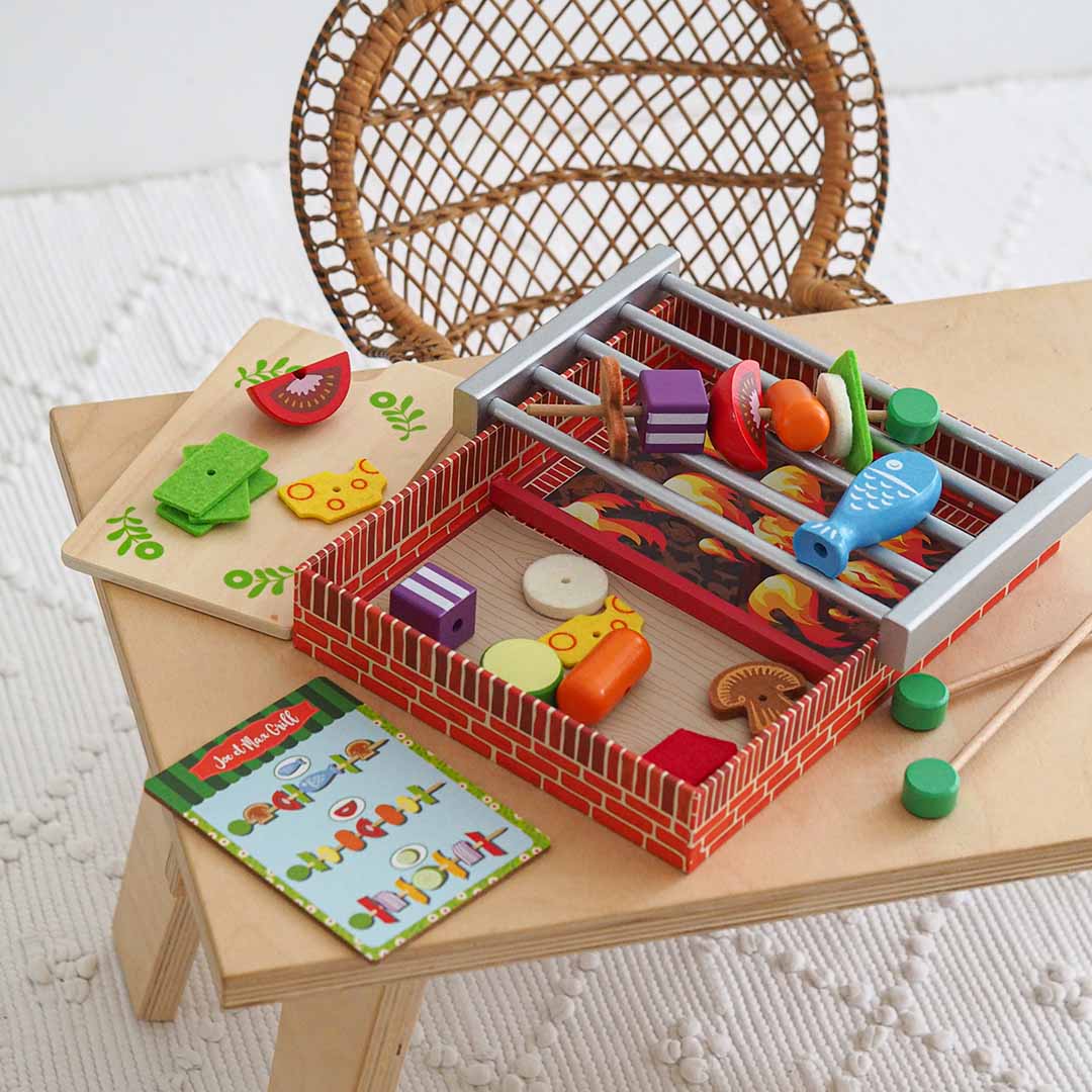 Djeco barbecue speelset op een houten tafeltje met de grill, snijplank en receptenkaart.