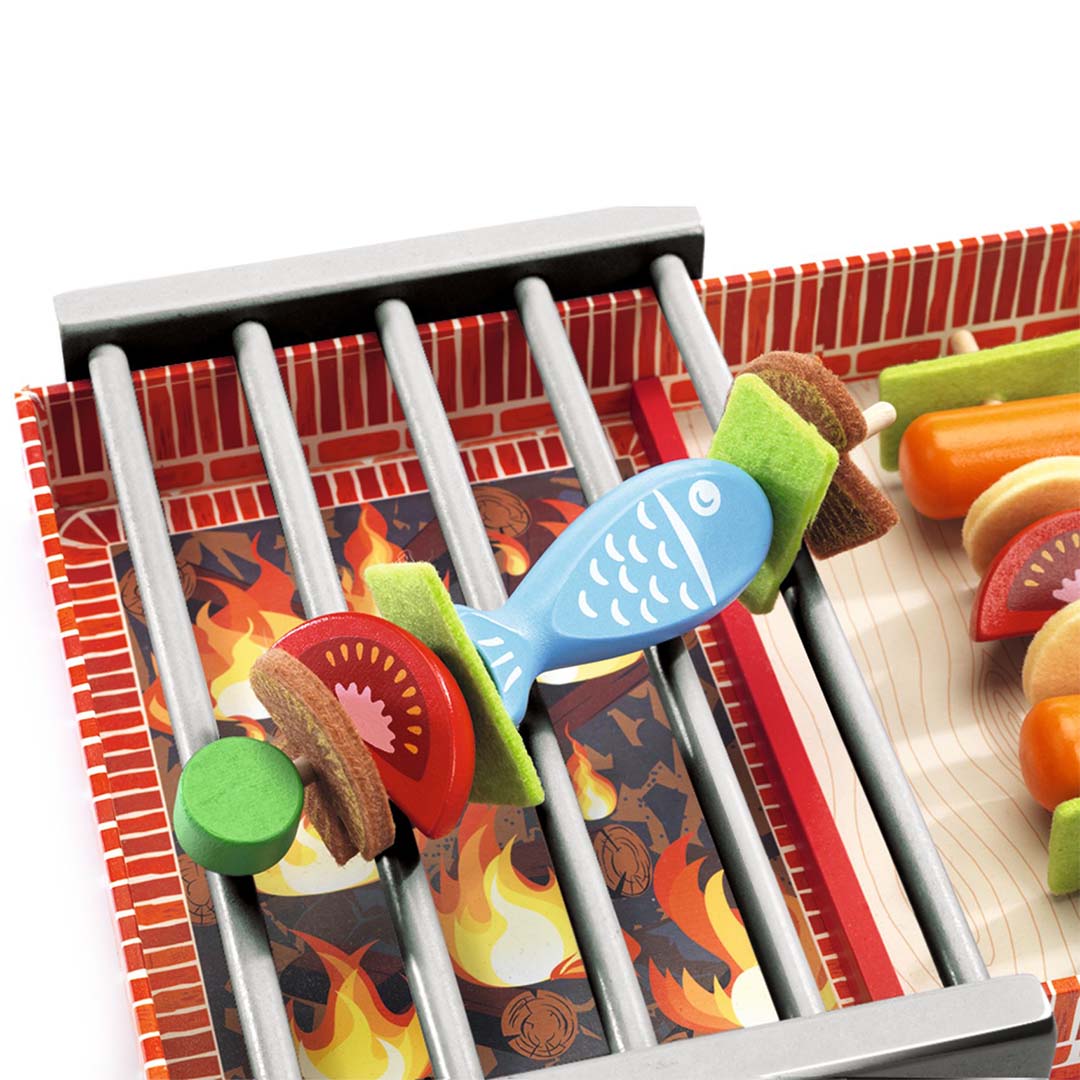 Detail van de Djeco barbecue speelset met een houten vis en groenten op een spies boven de grill.