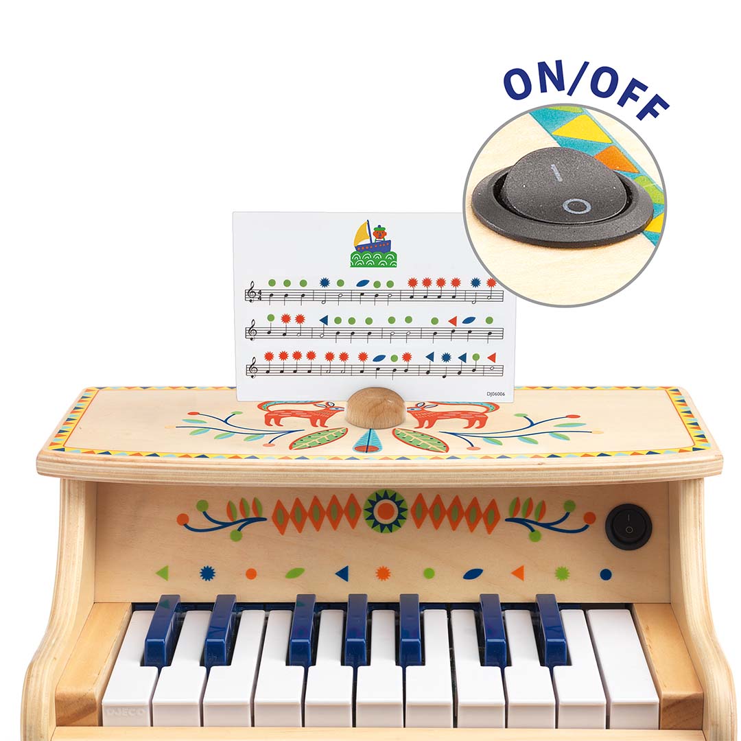 Bovenaanzicht van de Djeco elektronische piano met muziekvel en een detail van de aan/uit-knop.