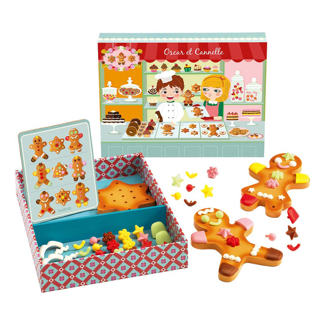 Djeco speelgoedset met twee versierde gingerbread koekjes, een open doos met onversierde koekjes en decoraties, en een bakkerij achtergrondkaart.