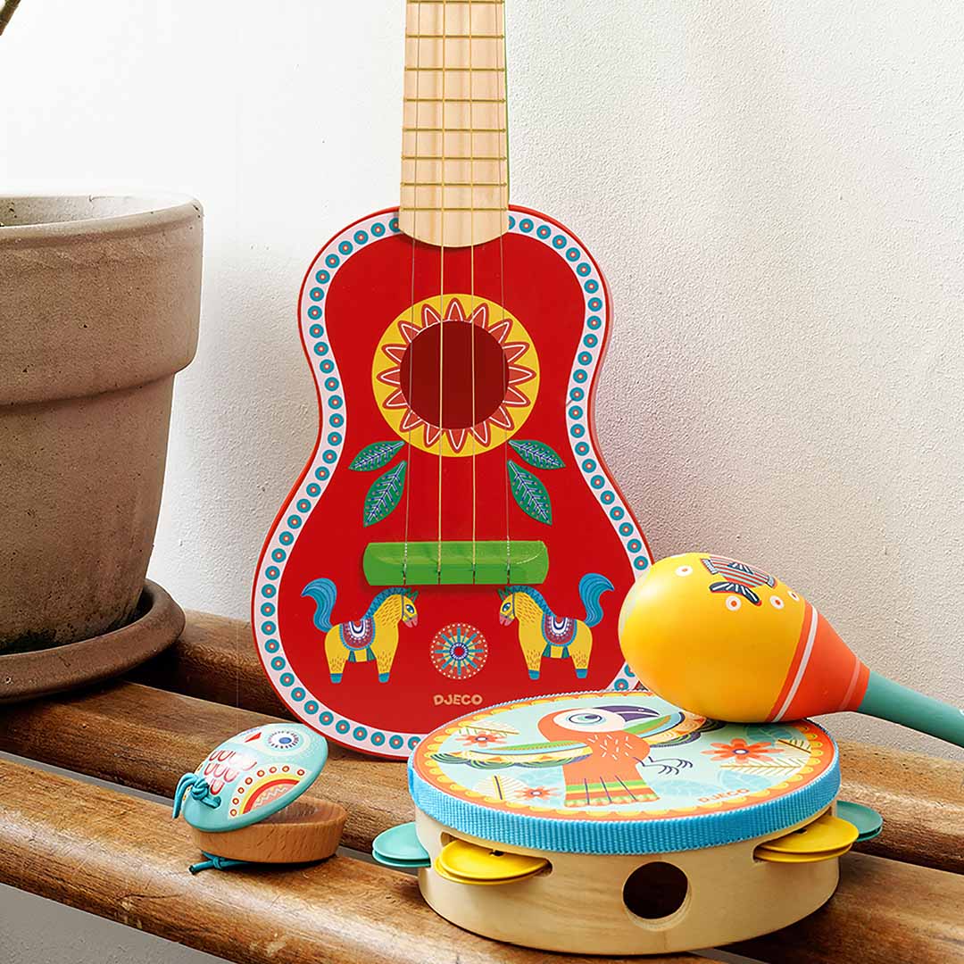 Djeco rode speelgoedgitaar met etnisch patroon, samen met een tamboerijn, maraca en castagnet op een bankje.