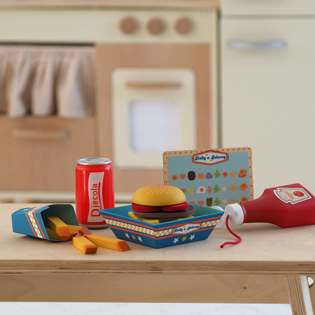 Djeco speelgoed fastfood set met frisdrank, frietjes, burger en ketchup op een houten tafel voor een speelgoedkeuken.