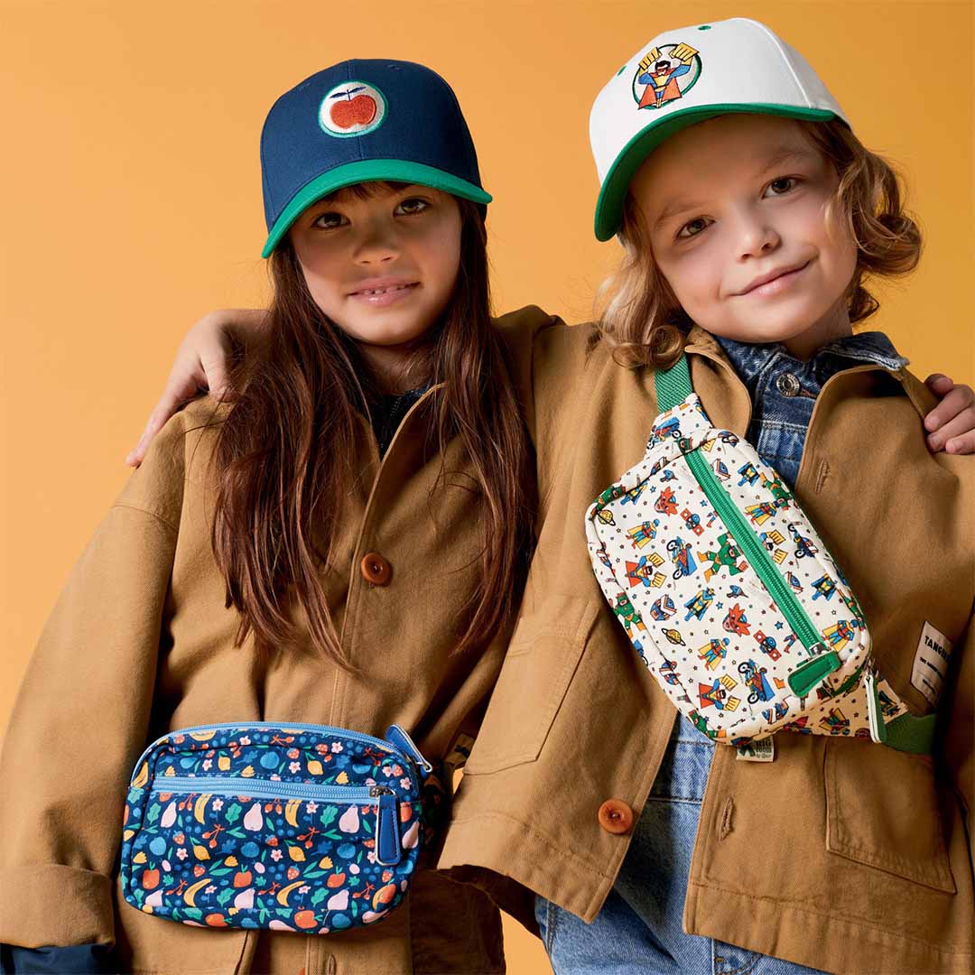 Twee kinderen dragen heuptassen, waarbij het meisje links de Djeco kinder heuptas met fruitpatroon draagt.