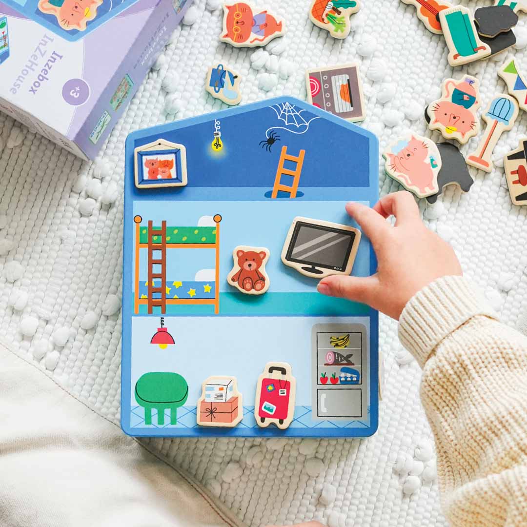 Een kinderhand plaatst een magnetische televisie in een kamer van het opengeklapte magnetische huisspel.
