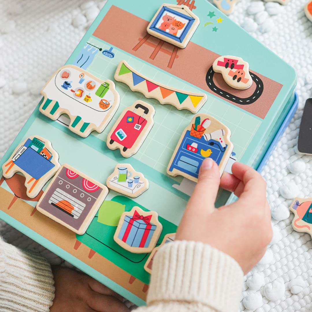 Een kinderhand plaatst een magnetisch cadeau op het opengeklapte magnetische huisspel.