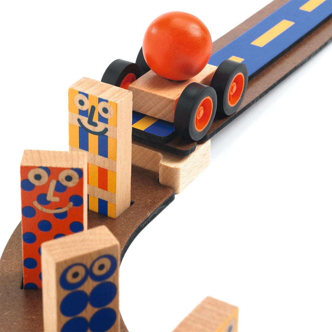 Detail van een houten autootje met oranje bal op een blauwe helling, met houten blokjes in de voorgrond.