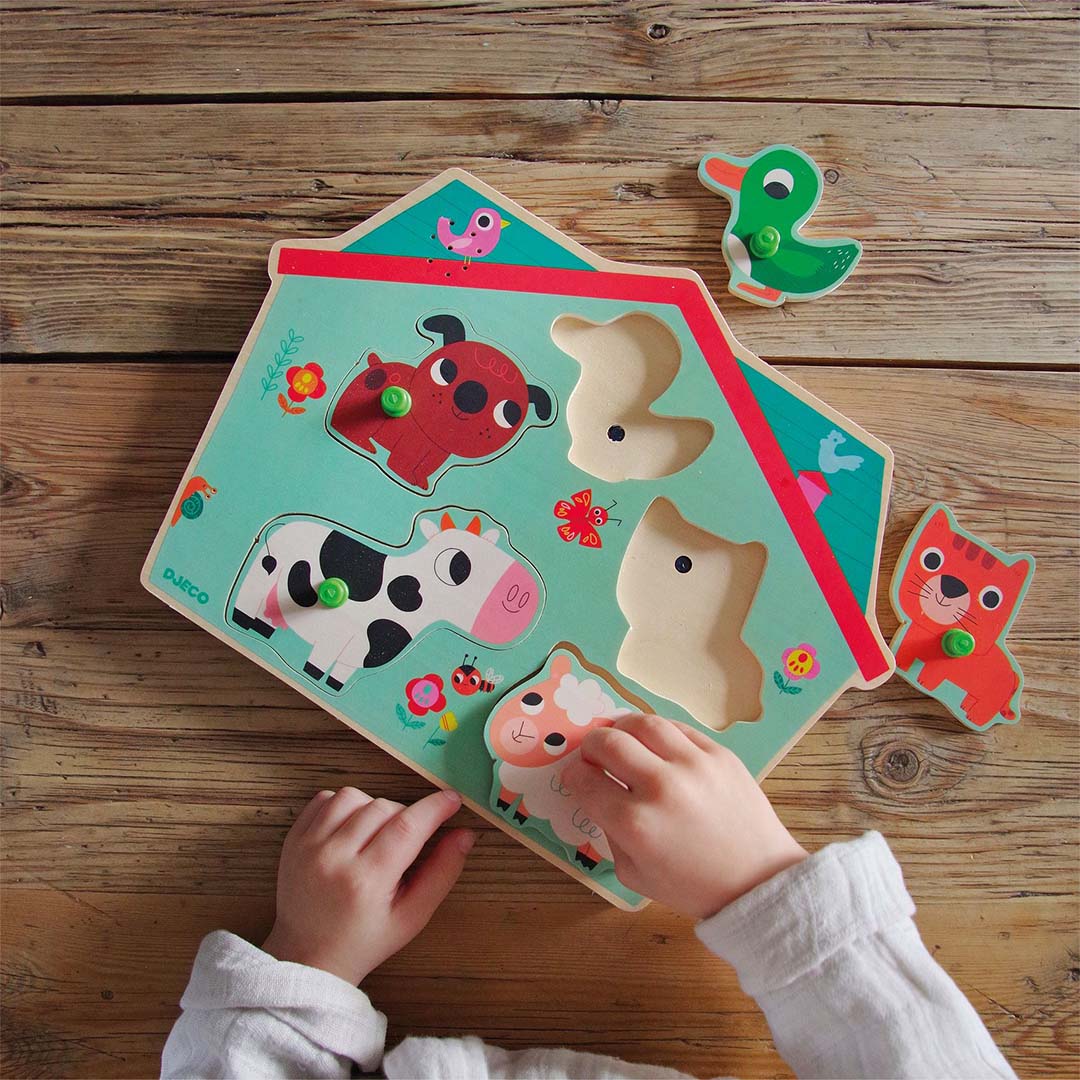 Kinderhanden spelen met de Djeco houten knoppuzzel met boerderijdieren.