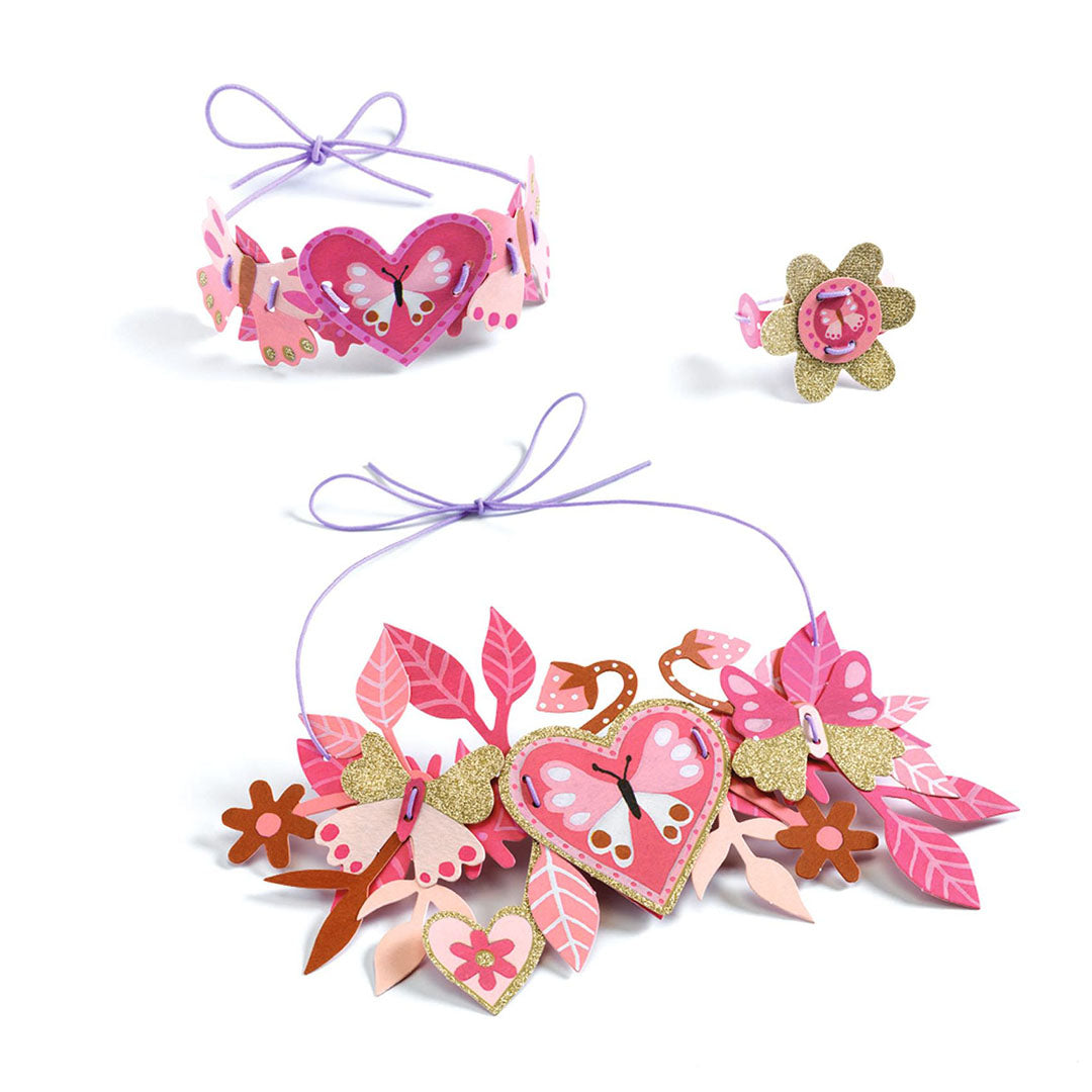 Een set van roze bloemen sieraden met harten en vlindermotieven, bestaande uit een ketting, armband en ring.